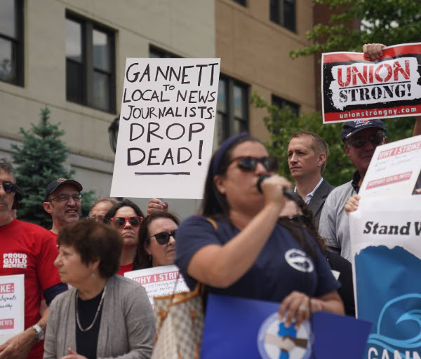 Union members gathered at a rally with a sign that reads, “Gannett to local news journalists: drop dead!”